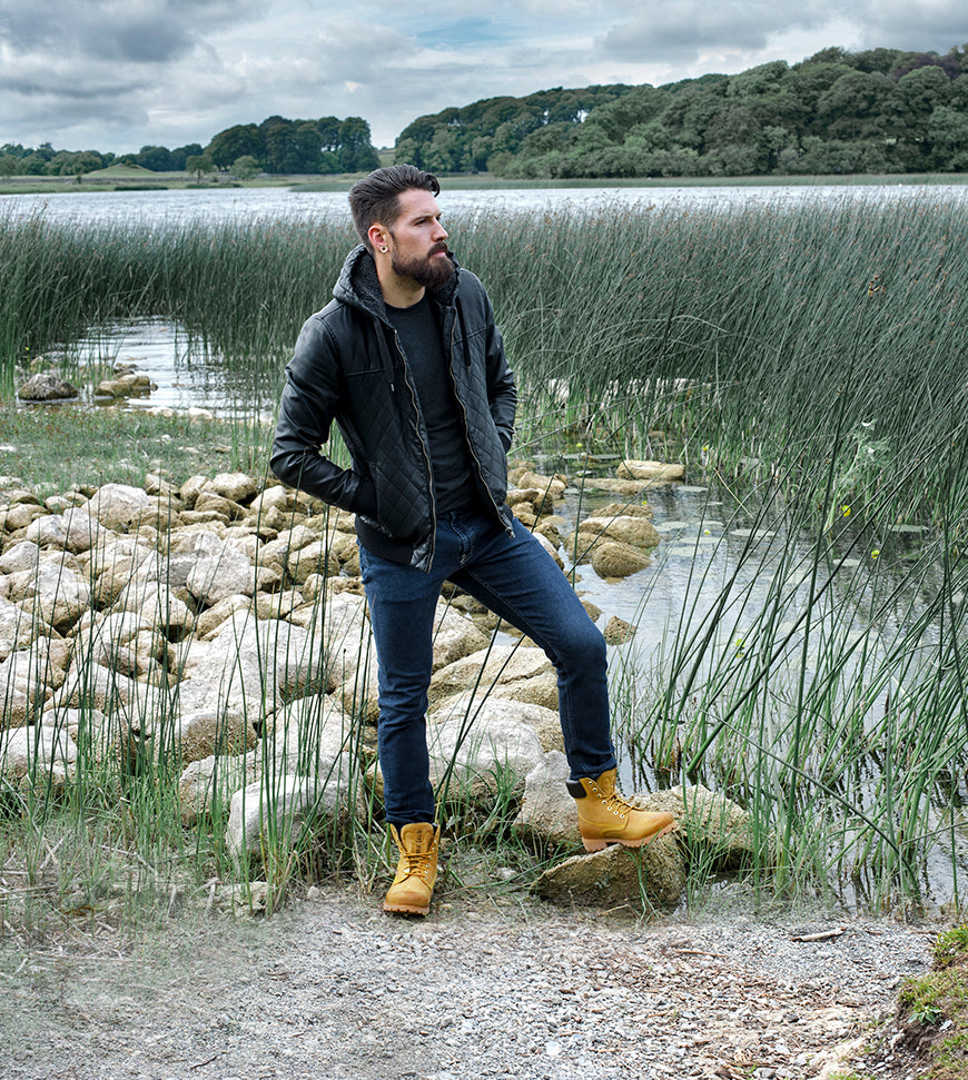 Chico con las botas icónicas de Panama Jack en unas piedras en la orilla de un lago